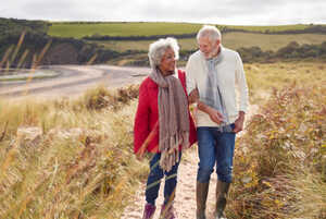 Older couple walking together through sand dunes on a winter beach holiday