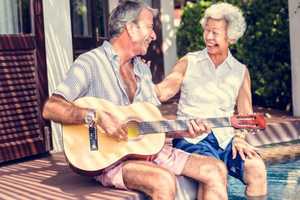 Elderly couple enjoying their retirement, sat in their garden while playing the guitar. 