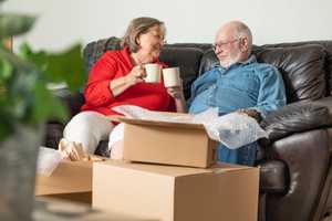 Older couple having a cuppa on the sofa, surrounded with moving boxes