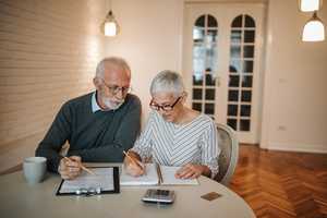 Senior couple sitting at a table in their home with paperwork and a calculator