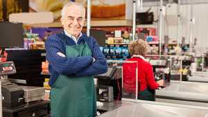 Older employee standing at a supermarket checkout