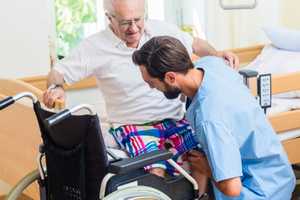 Care home resident being helped to move from wheelchair to bed