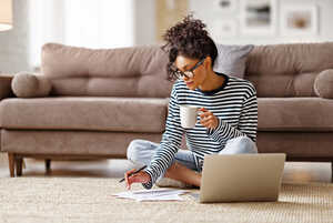 Young woman sitting at home, checking paperwork with a hot drink